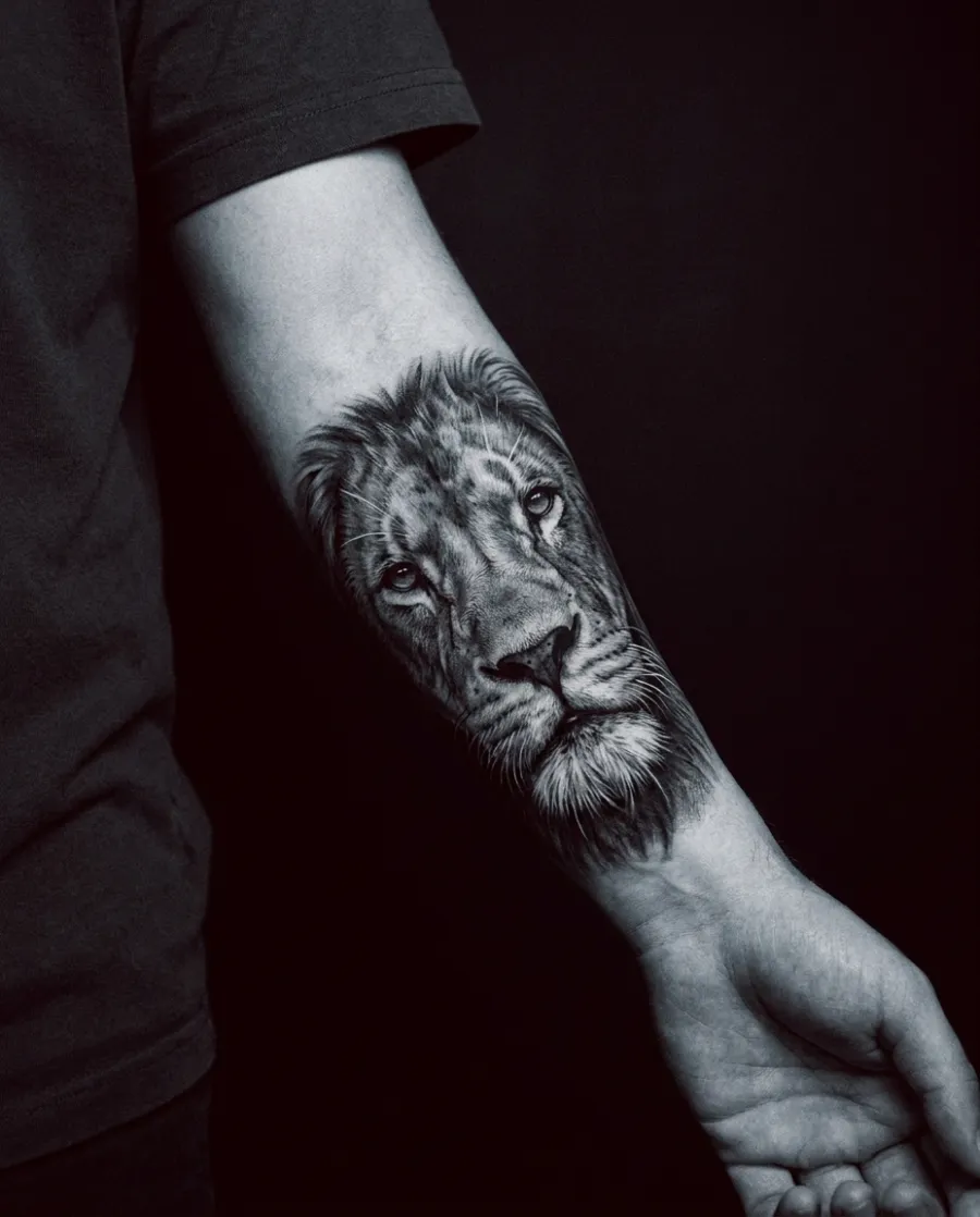 An extreme-detail black-and-grey realism tattoo of a lion's face on a forearm.