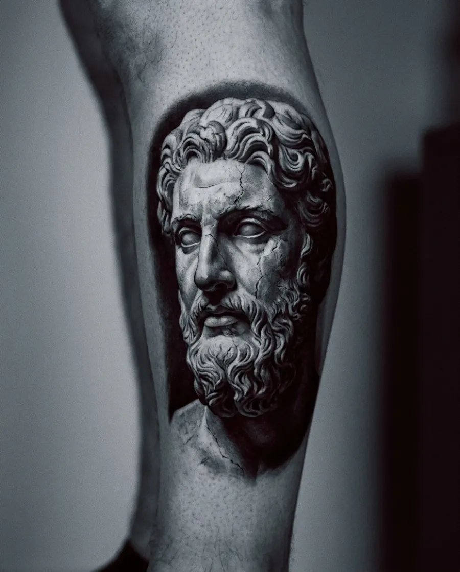 A black-and-grey realism tattoo of a classical marble statue's face on a calf.