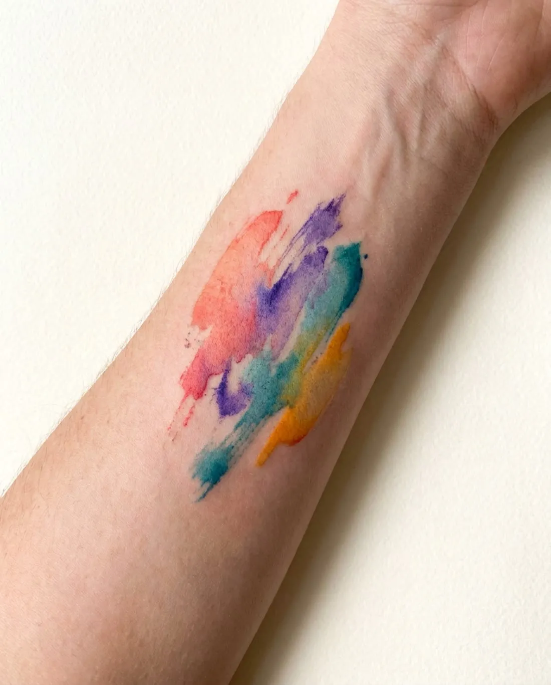 Abstract brushstroke watercolor tattoo in coral, violet and teal on a wrist