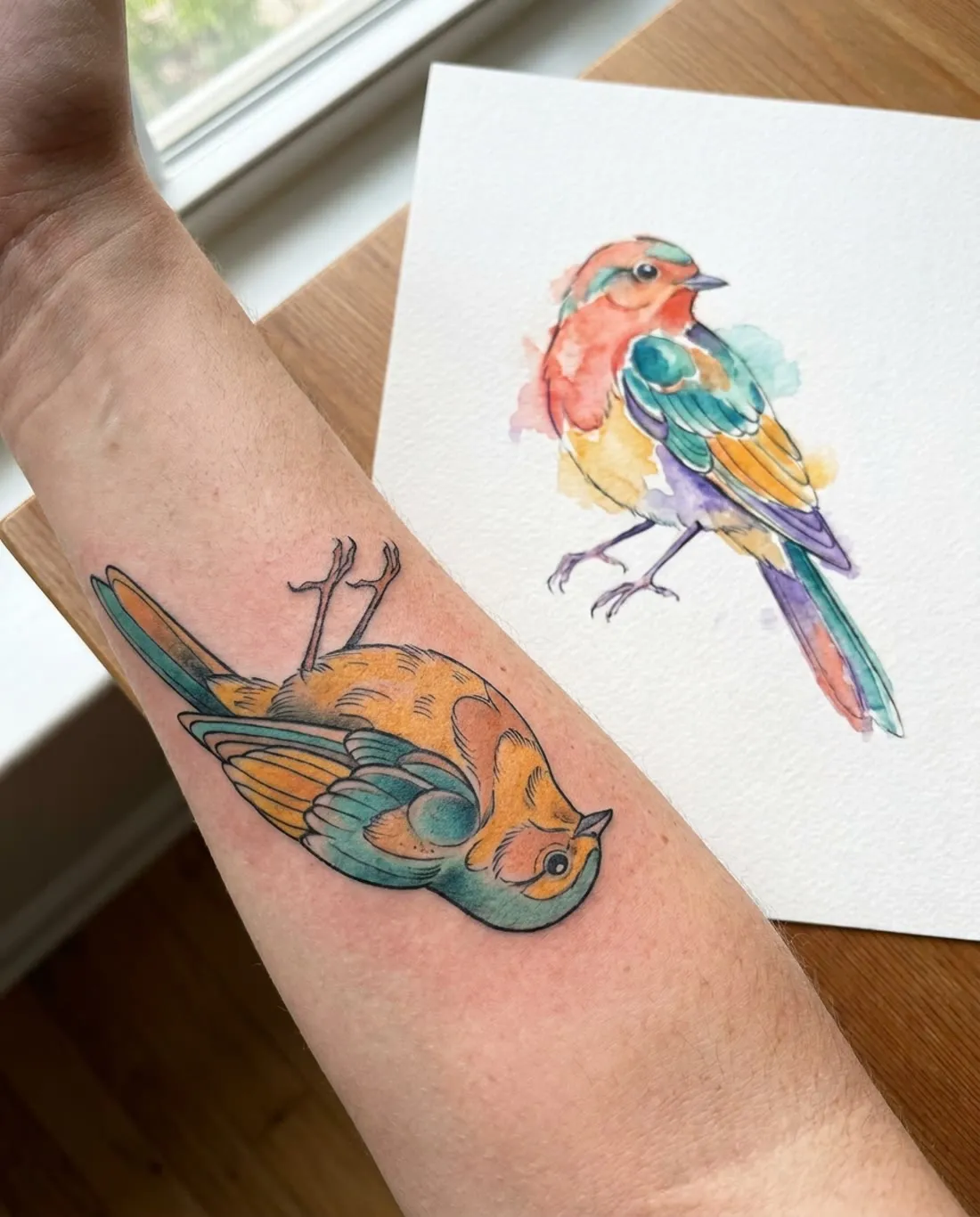 Illustrative color songbird tattoo with washed color on a forearm