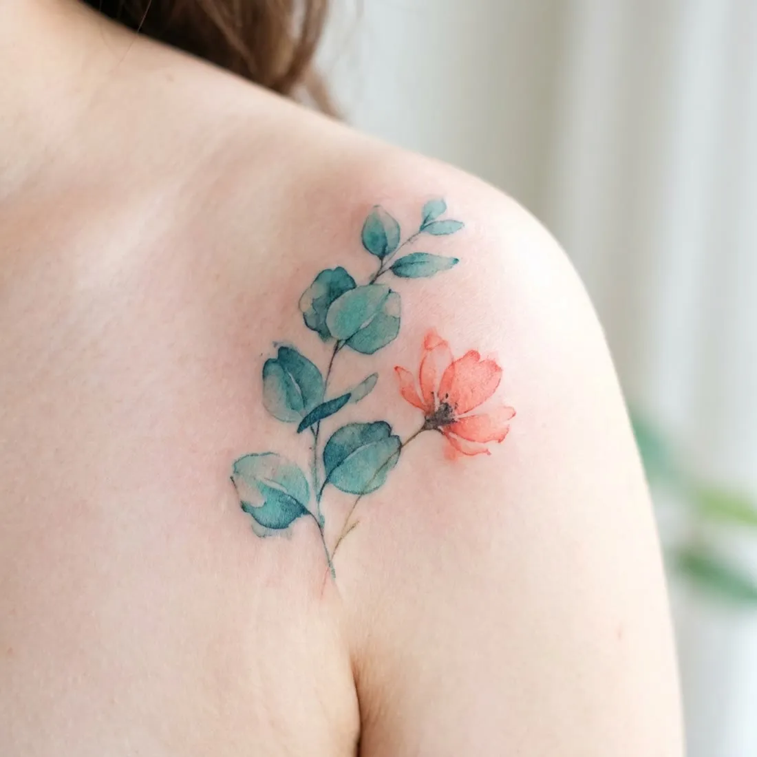 Delicate watercolor botanical tattoo in teal and coral on a shoulder