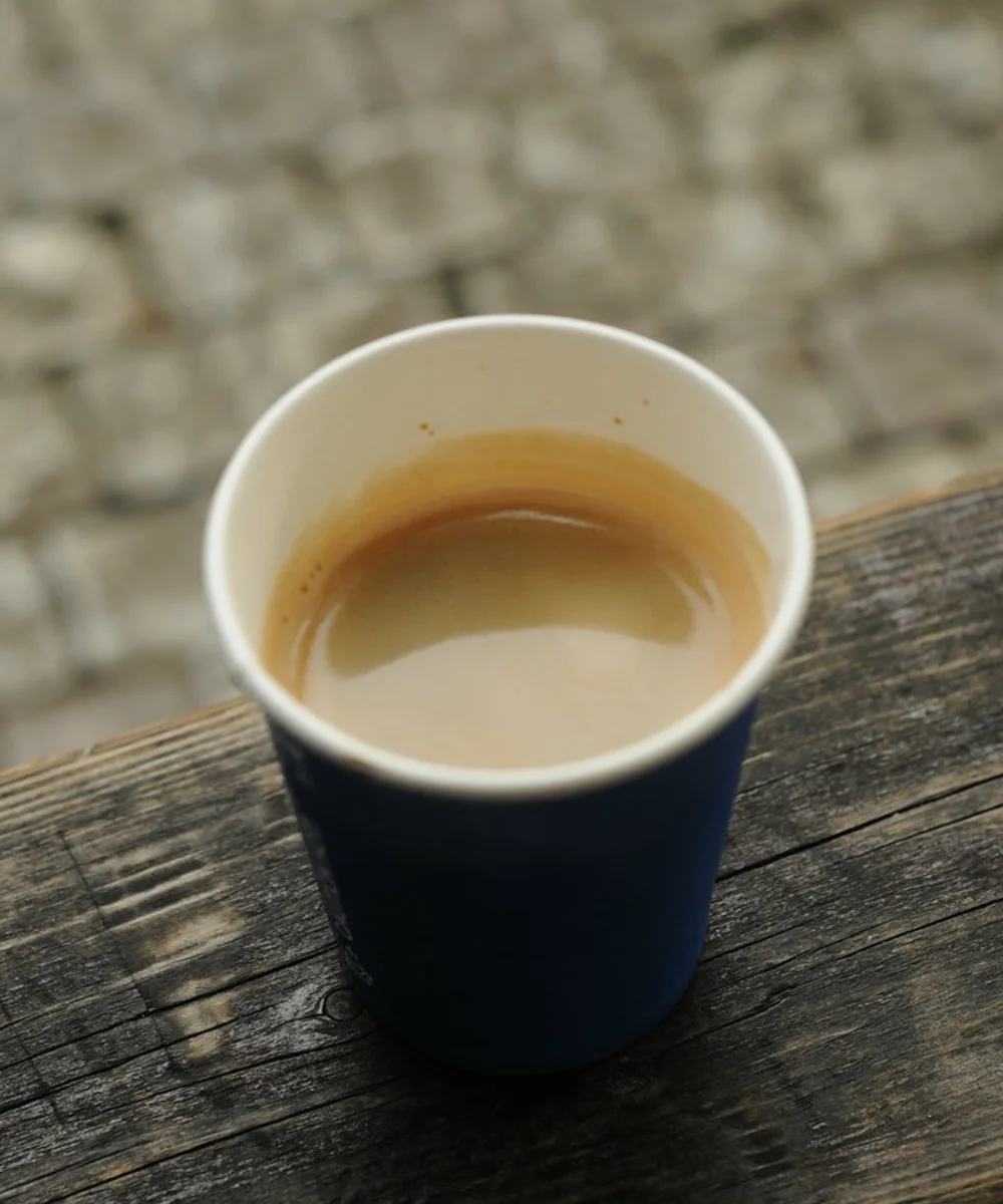 A flat white in a blue cup on a weathered wood rail